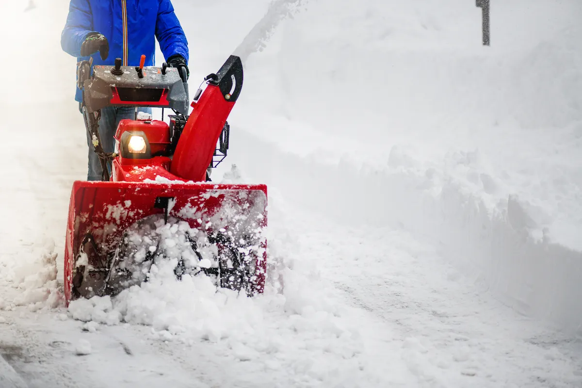 Person clearing snow in on walkway using a red snow blower